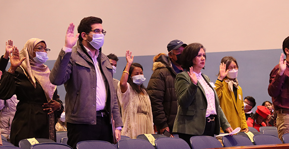 New citizens raising their hands for oath in Mount St. Joseph University Theatre. 