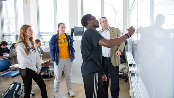 finance students in classroom writing on board with professor