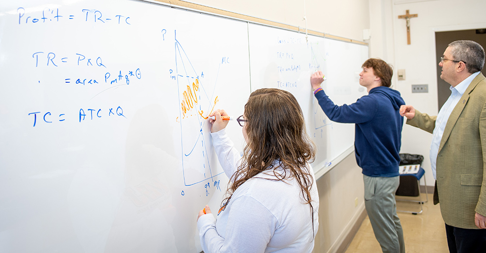 business students in classroom writing on dry erase board.