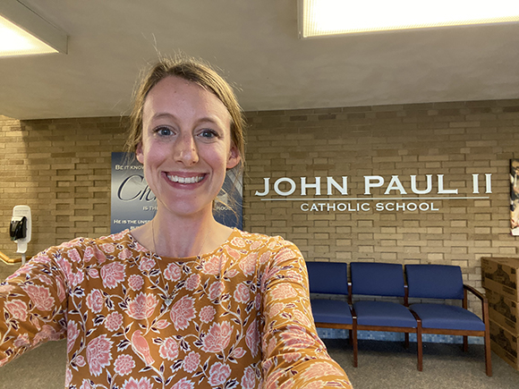 photo of teacher standing in front of school sign