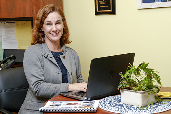 MSJ professor using laptop and smiling