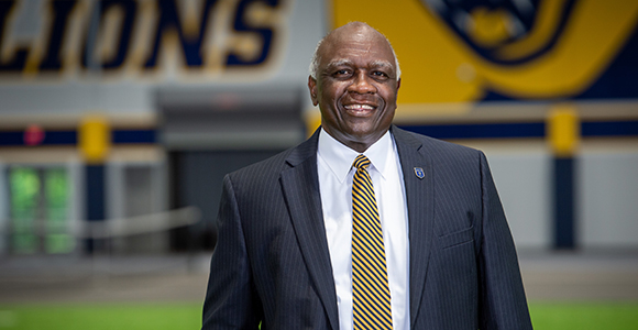 president H. James Williams standing and smiling in front of centennial fieldhouse indoor track