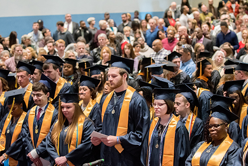 graduates in regalia standing in harrington gym for commencement.