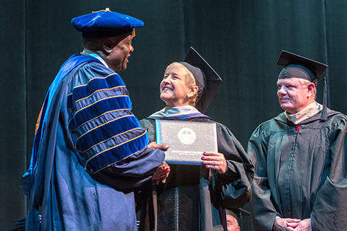 adult student receiving diploma on stage.